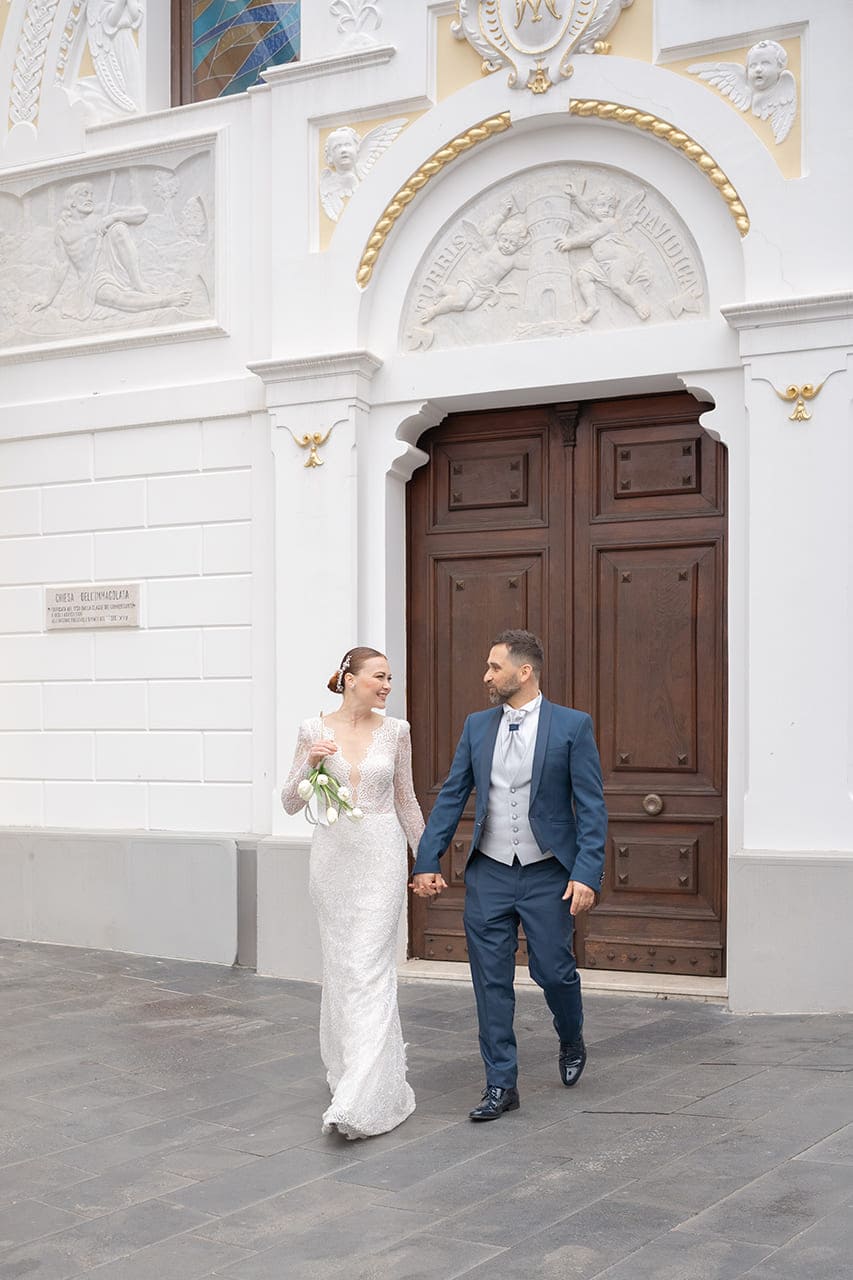Sposi mano nella mano davanti alla chiesa in piazza a Pizzo Calabro durante un matrimonio editoriale